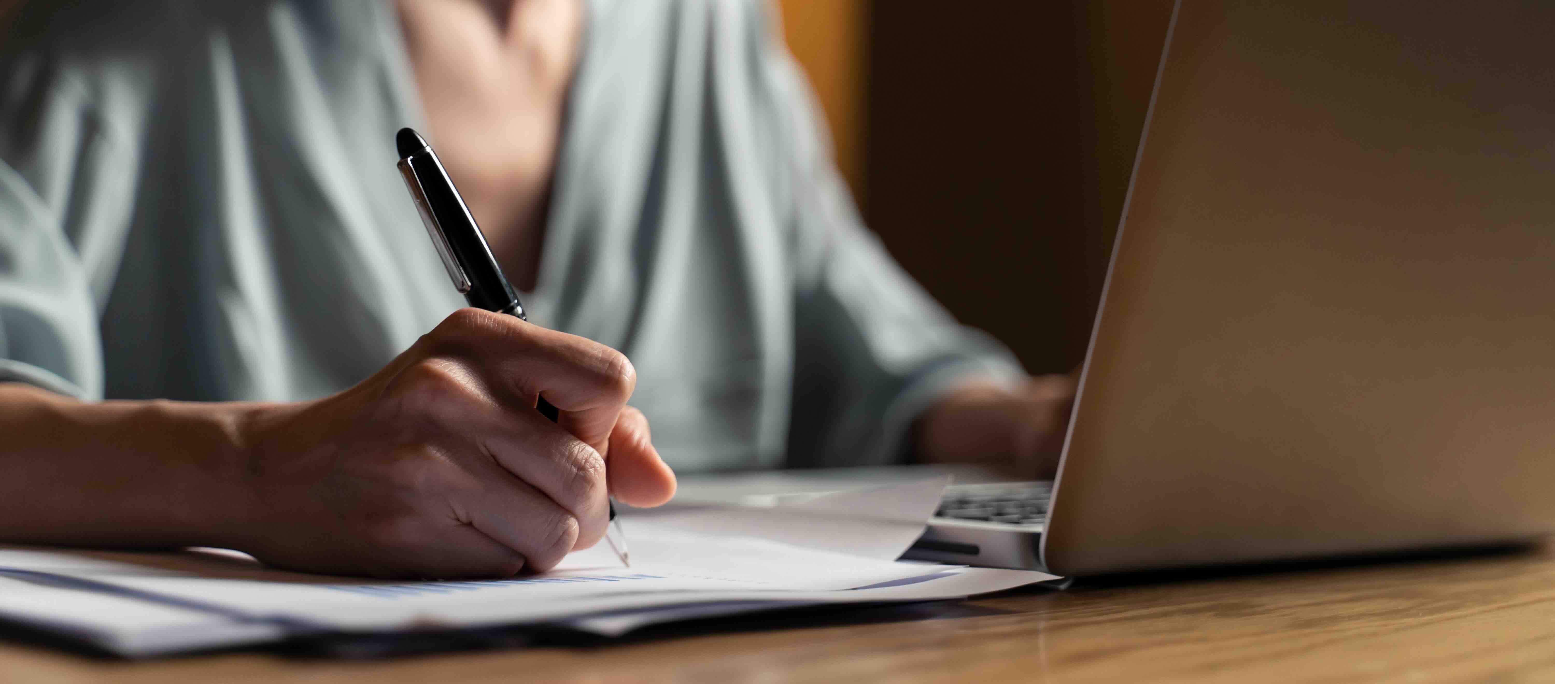 A researcher reviewing documentation while tracking equipment utilization on a laptop, representing how QReserve links resource usage to project codes for university grant compliance and audit readiness.